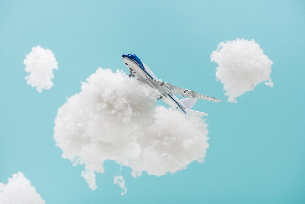 παιχνίδι αεροπλάνο που φέρουν μεταξύ λευκό αφράτο σύννεφα από μαλλί βαμβάκι που απομονώνονται σε μπλε - Φωτογραφία, εικόνα