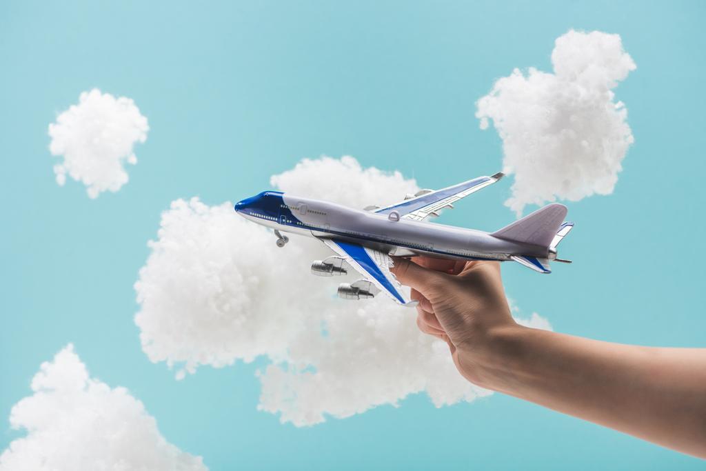 cropped view of woman playing with toy plane among white fluffy clouds made of cotton wool isolated on blue - Photo, Image