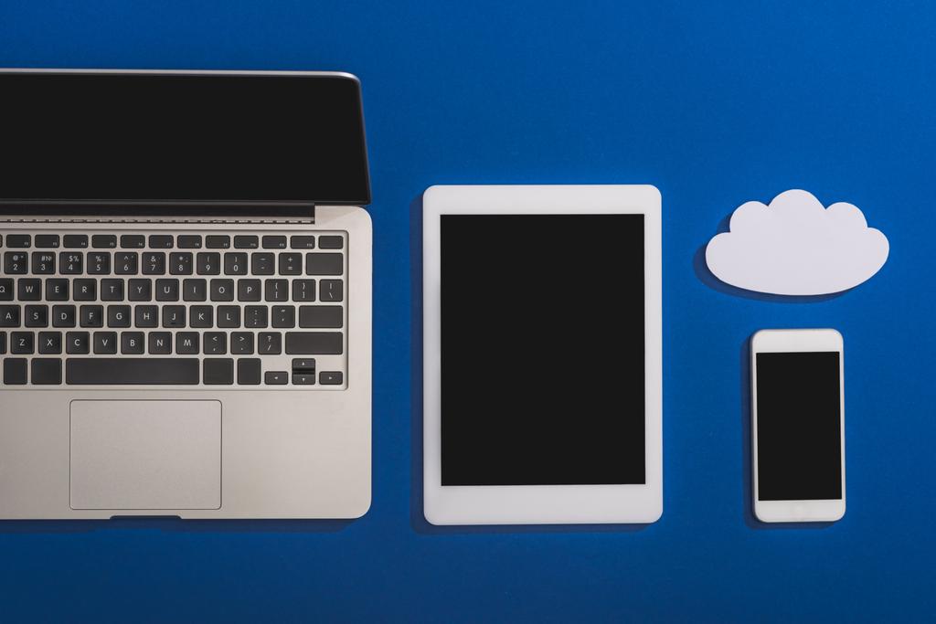 vista superior de la nube vacía de papel blanco cerca de la computadora portátil, teléfono inteligente y tableta digital con pantalla en blanco aislada en azul
 - Foto, Imagen