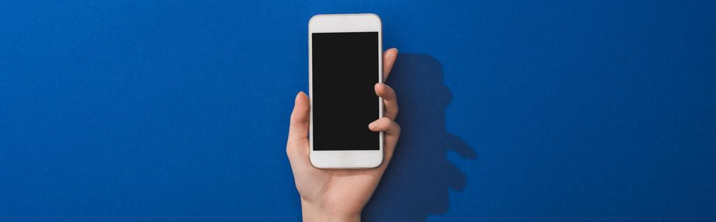 vista recortada de la mujer sosteniendo teléfono inteligente sobre fondo azul, plano panorámico
 - Foto, imagen