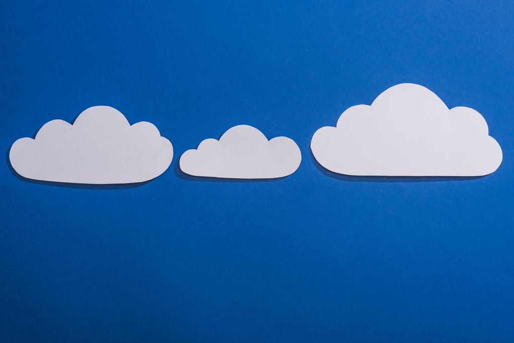 Beyaz kağıdın üst görünümü mavi arkaplanda bulutları keser - Fotoğraf, Görsel