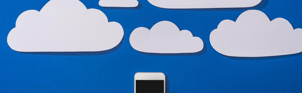 κορυφαία άποψη του λευκού χαρτιού κομμένα σύννεφα και smartphone σε μπλε φόντο, πανοραμική λήψη - Φωτογραφία, εικόνα