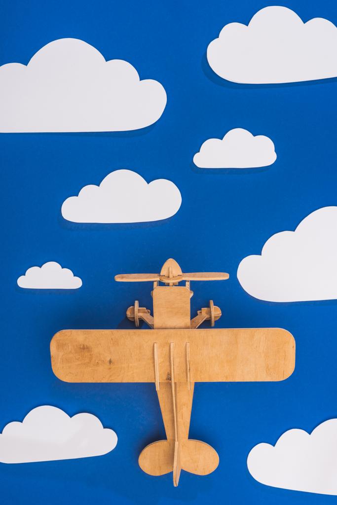 top view of wooden toy plane in blue sky with paper cut white clouds - Photo, Image