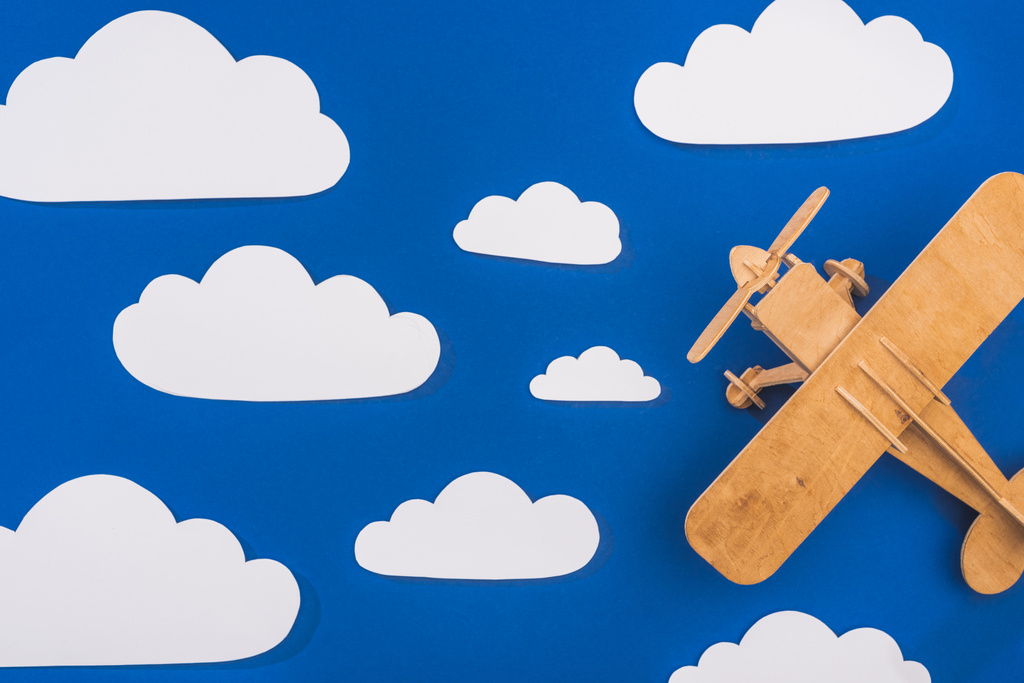 Draufsicht auf Holzspielzeugflugzeug in blauem Himmel mit papiergeschnittenen weißen Wolken - Foto, Bild