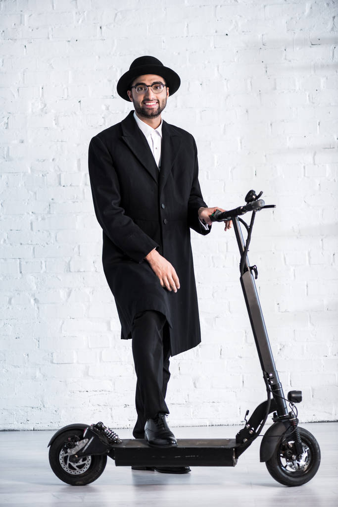 hombre judío guapo y sonriente en gafas de pie cerca de scooter
 - Foto, imagen