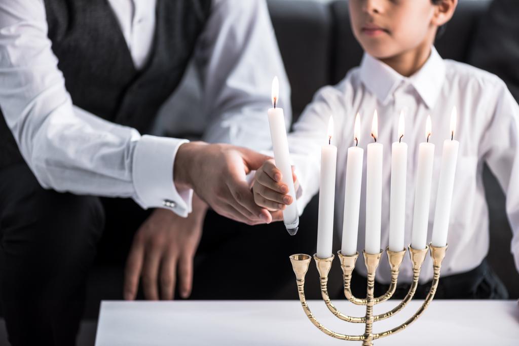 Ausgeschnittene Ansicht von jüdischem Vater und Sohn mit Kerze in Wohnung  - Foto, Bild