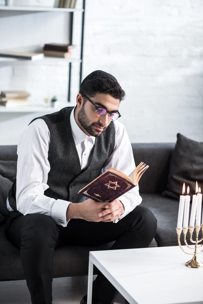 knappe joodse man in bril lezen tanakh in appartement  - Foto, afbeelding