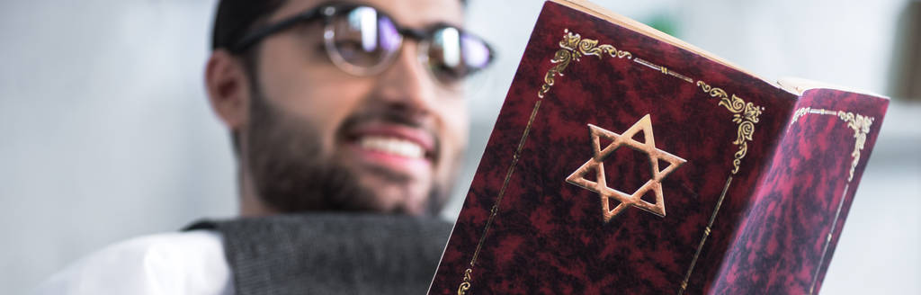 πανοραμικό πλάνο του χαμογελαστού Εβραίου με γυαλιά που διαβάζει τανάκ  - Φωτογραφία, εικόνα