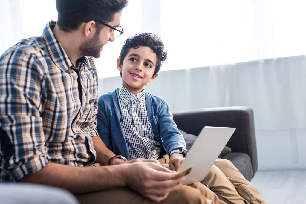 padre ebreo e figlio sorridente utilizzando il computer portatile in appartamento
  - Foto, immagini