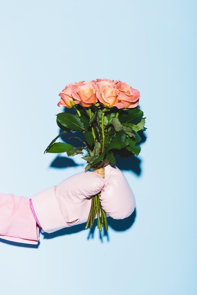 cropped view of woman in boxing glove holding bouquet on blue background  - Photo, Image