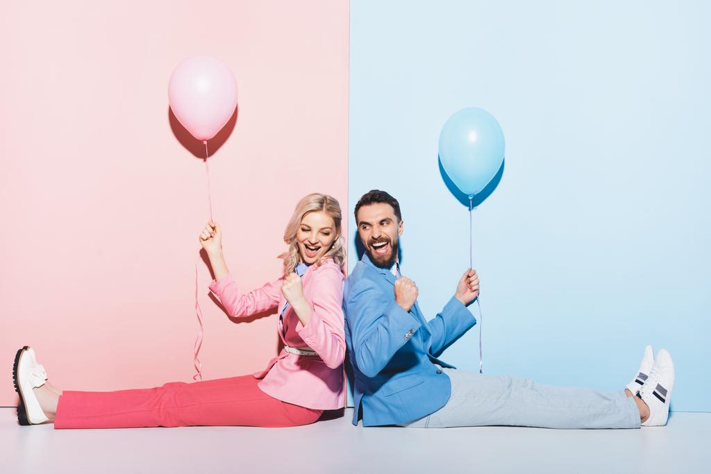 πλάτη με πλάτη θέα χαμογελαστή γυναίκα και όμορφος άντρας με μπαλόνια που δείχνουν ναι χειρονομία σε ροζ και μπλε φόντο  - Φωτογραφία, εικόνα