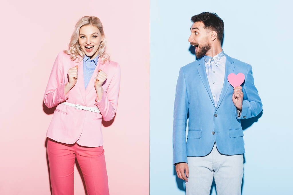 shocked woman and handsome man with heart-shaped card on pink and blue background  - Photo, Image
