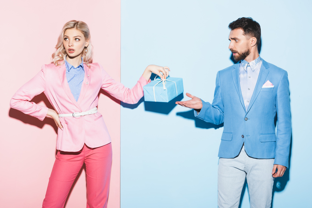 donna attraente che tiene regalo e bell'uomo che punta con mano su sfondo rosa e blu
  - Foto, immagini