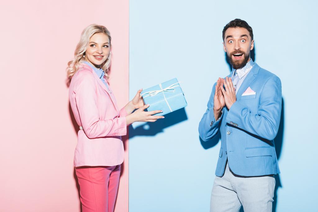 mujer atractiva dando regalo al hombre sorprendido sobre fondo rosa y azul
  - Foto, imagen