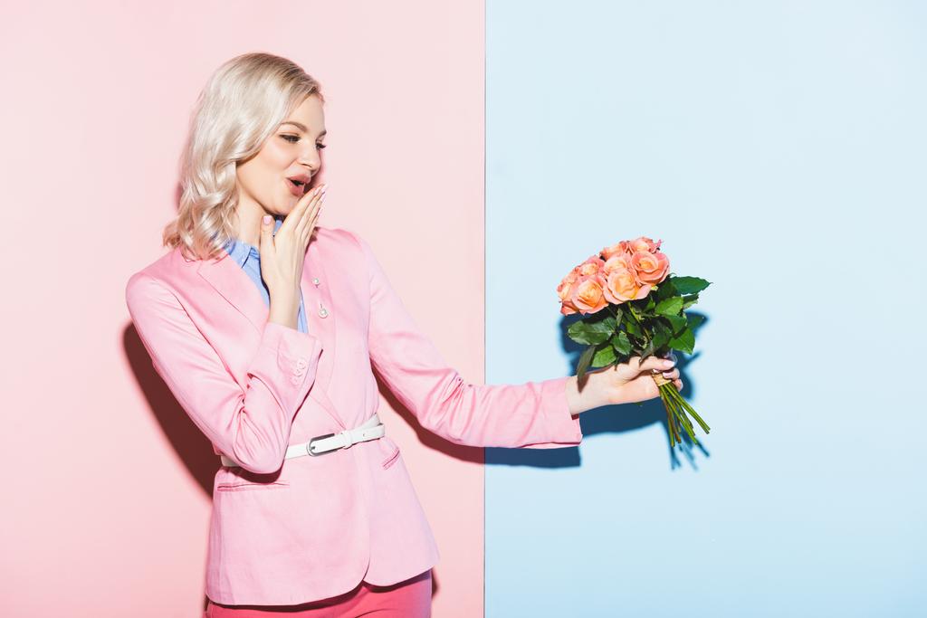ピンクと青の背景に花束を持ったショックを受けた女性 - 写真・画像