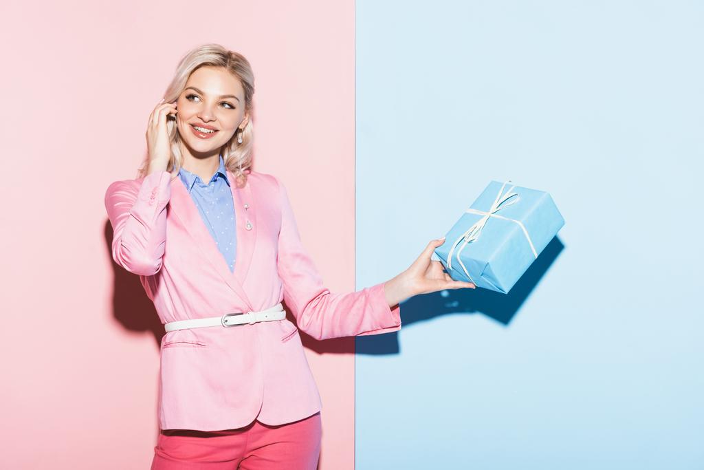 mosolygós nő gazdaság ajándék doboz rózsaszín és kék háttér  - Fotó, kép
