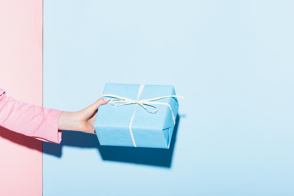 cropped view of woman holding gift box on pink and blue background  - Photo, Image