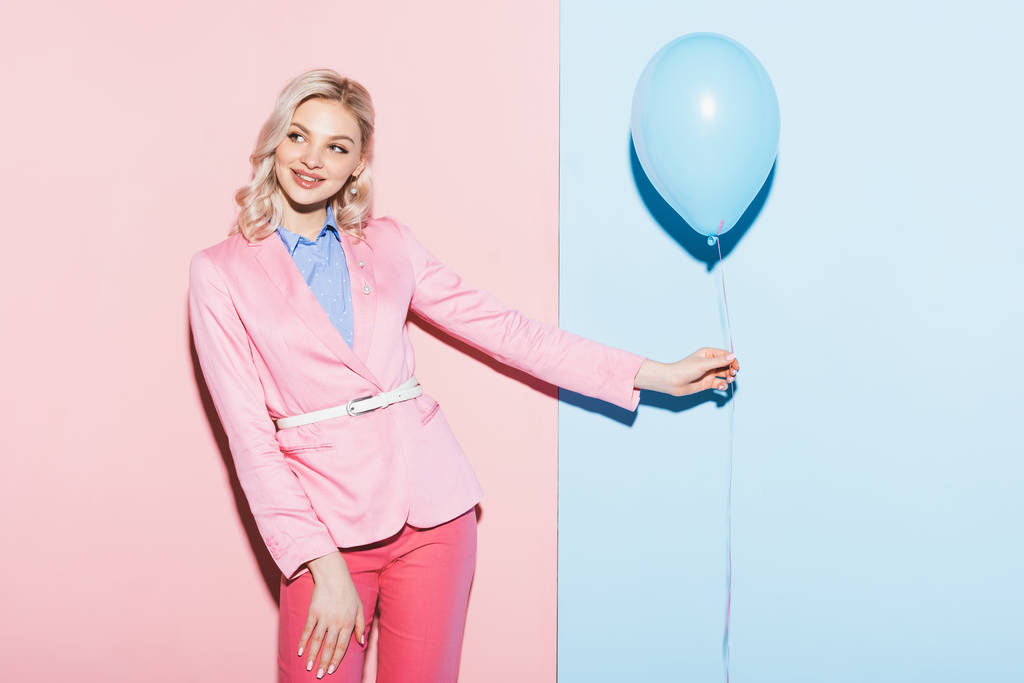χαμογελαστή γυναίκα κρατώντας μπαλόνι σε ροζ και μπλε φόντο  - Φωτογραφία, εικόνα
