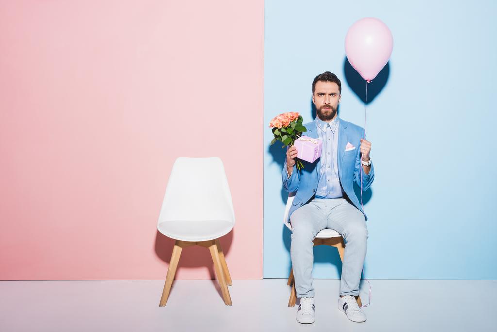 όμορφος και λυπημένος άνδρας κρατώντας μπαλόνι, δώρο και σε μπουκέτο μπλε και ροζ φόντο  - Φωτογραφία, εικόνα