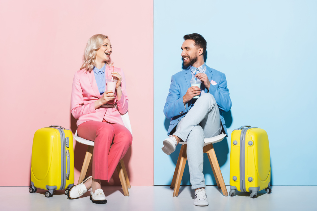 usmívající se žena a pohledný muž držící koktejly na růžovém a modrém pozadí  - Fotografie, Obrázek
