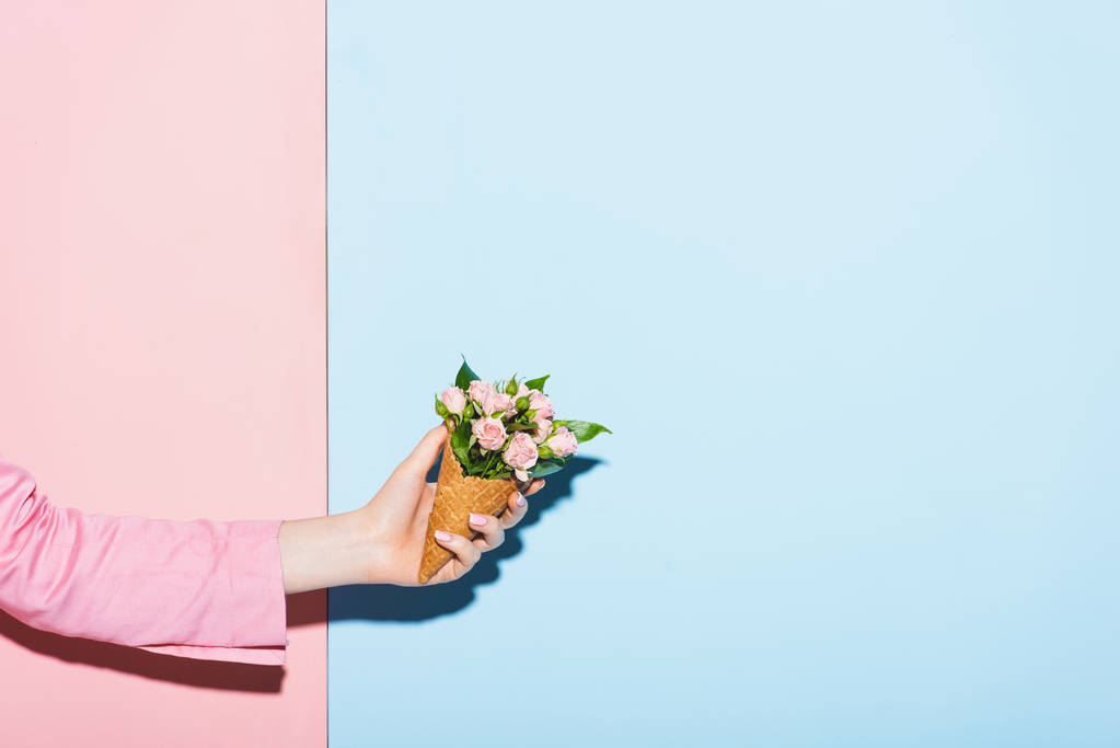 ピンクと青の背景で花束を持っている女性のクロップドビュー  - 写真・画像