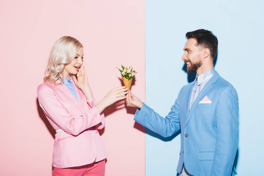 ピンクと青の背景を持つショックを受けた女性に花束を贈る笑顔の男  - 写真・画像