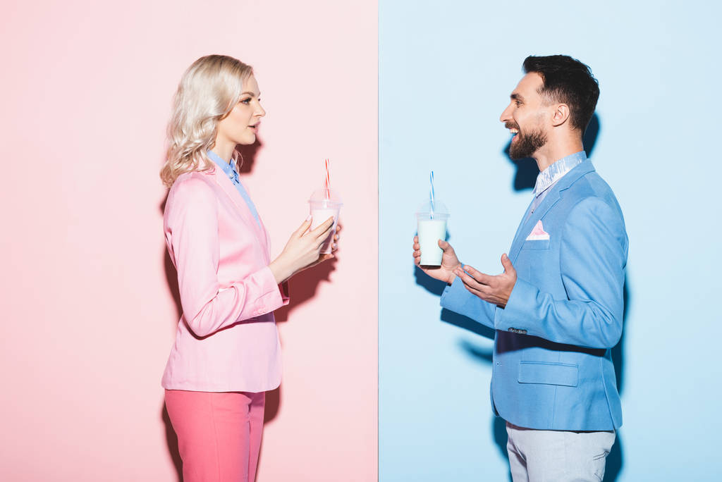 вид збоку привабливої жінки і усміхнений чоловік тримає коктейлі на рожевому і синьому фоні
  - Фото, зображення