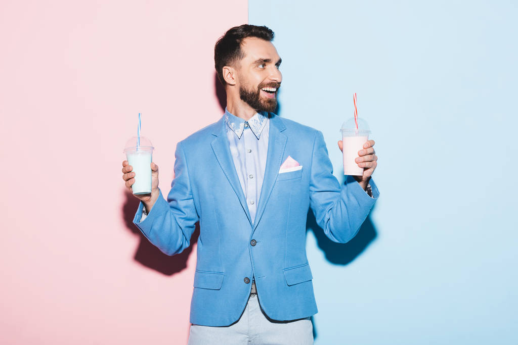 hombre sonriente sosteniendo cócteles sobre fondo rosa y azul
  - Foto, Imagen
