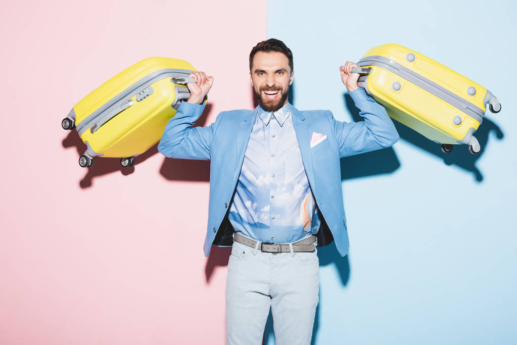 smiling man holding travel bags on pink and blue background  - Photo, Image