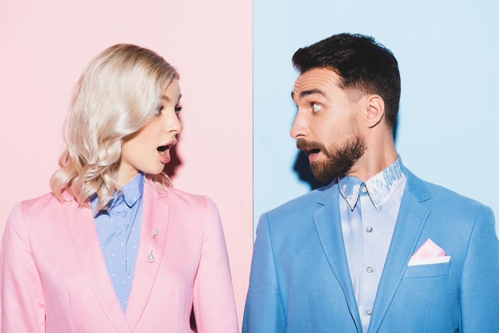 schockierte Frau und gutaussehender Mann schauen einander auf rosa und blauem Hintergrund an  - Foto, Bild