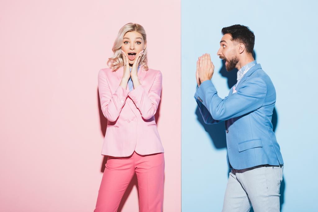 geschokte vrouw en knappe man kijken naar haar op roze en blauwe achtergrond  - Foto, afbeelding