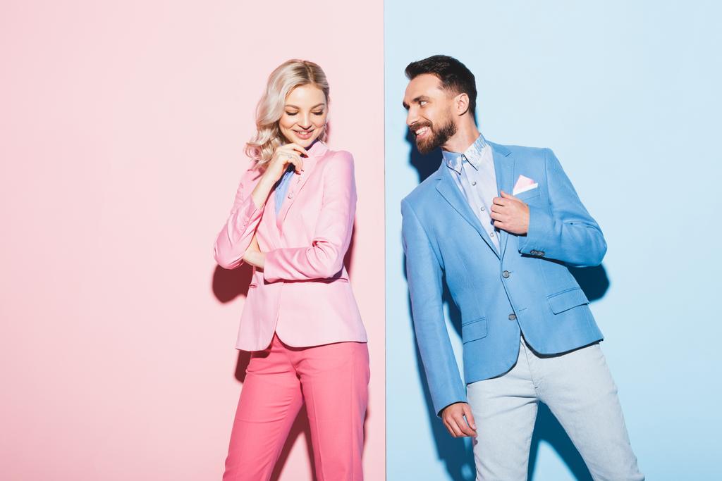 atraktivní žena a usmívající se muž při pohledu na ni na růžovém a modrém pozadí  - Fotografie, Obrázek