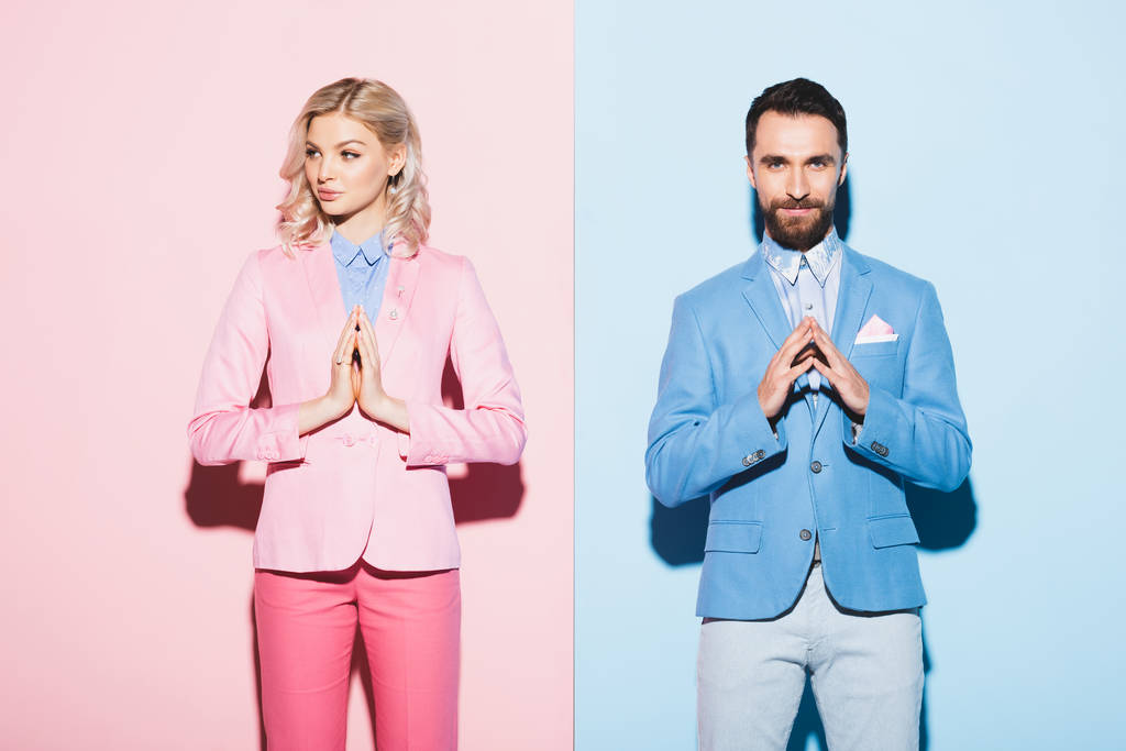 ピンクと青の背景で手を祈る魅力的な女性と笑顔の男  - 写真・画像