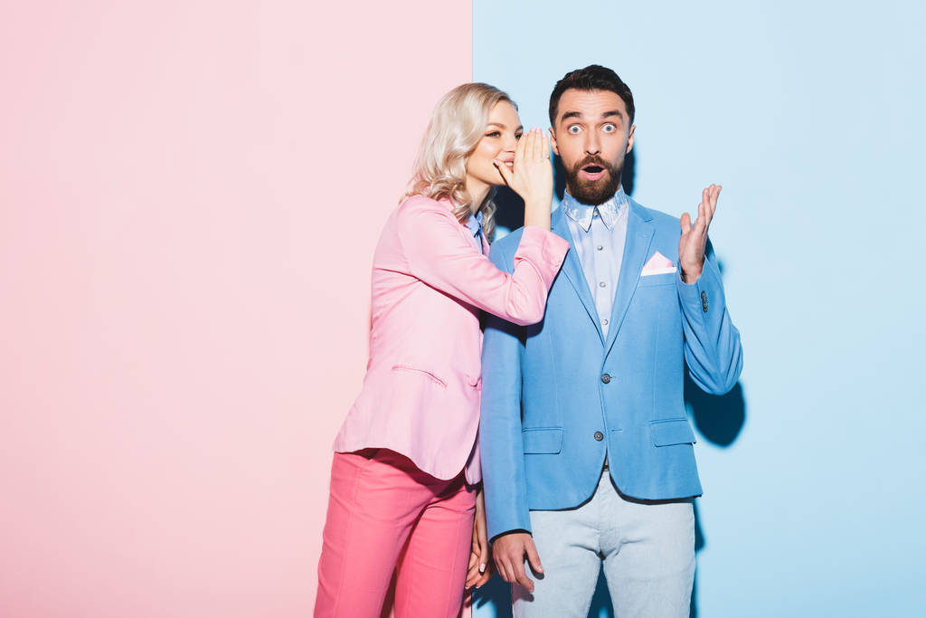 attraktive Frau verrät schockiertem Mann Geheimnis auf rosa und blauem Hintergrund  - Foto, Bild