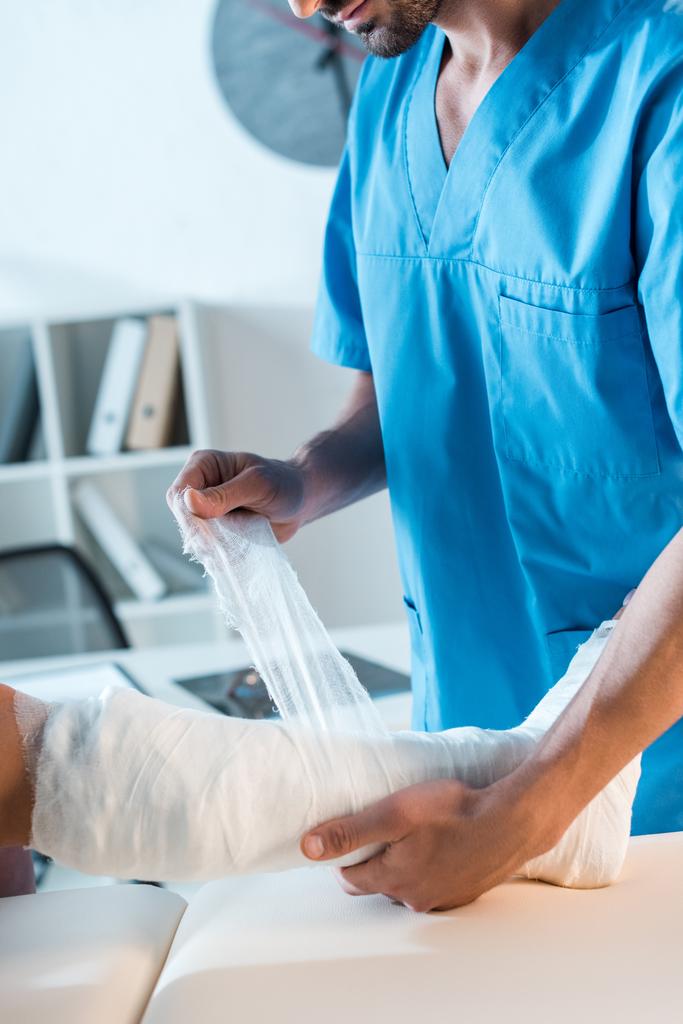 vue recadrée de l'orthopédiste mettant bandage sur jambe fracturée de la femme
  - Photo, image