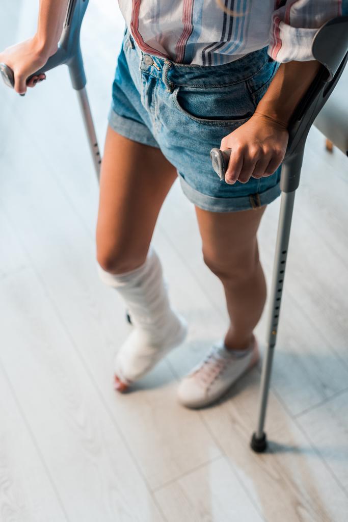 обрезанный вид переломанной женщины, держащей костыли, стоя в клинике
  - Фото, изображение