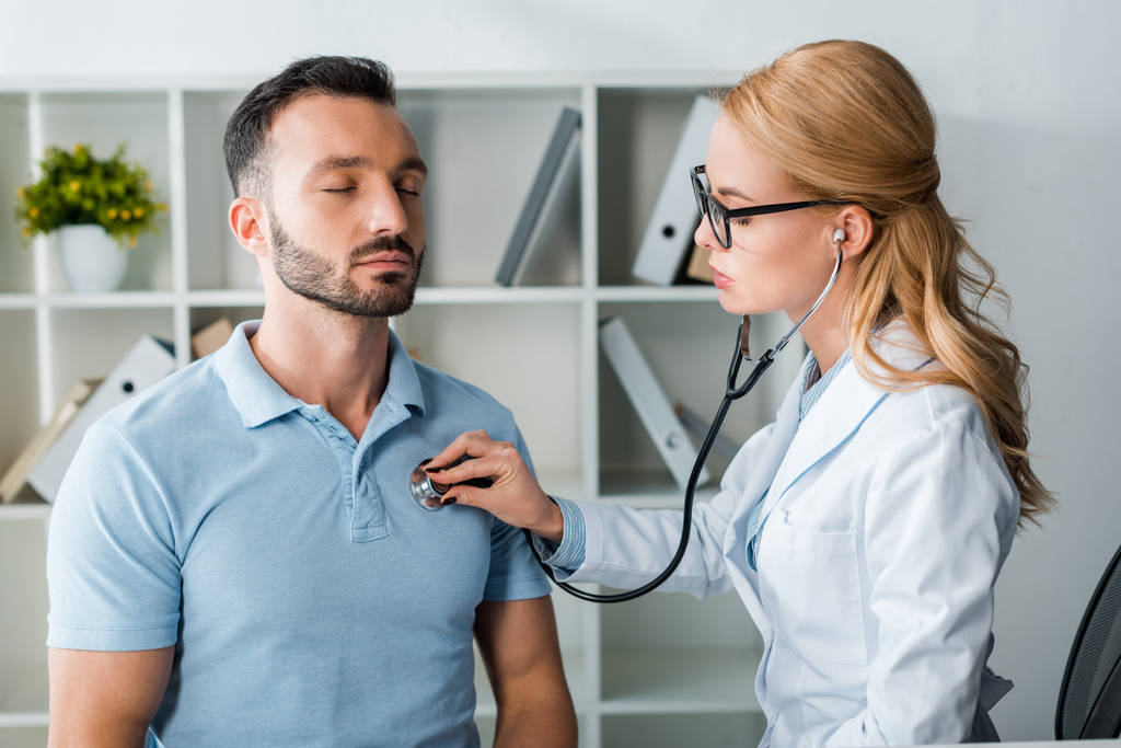 attractive doctor in glasses examining handsome man with closed eyes - Photo, Image