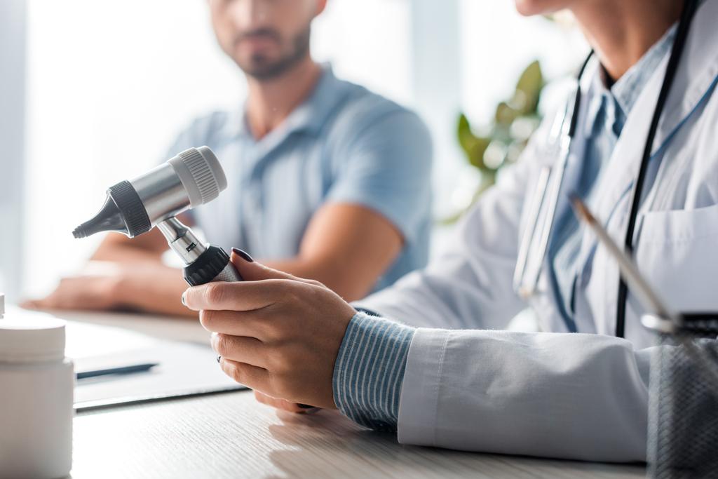 Ausgeschnittener Blick auf Arzt, der Otoskop in der Nähe von Mann in Klinik hält  - Foto, Bild