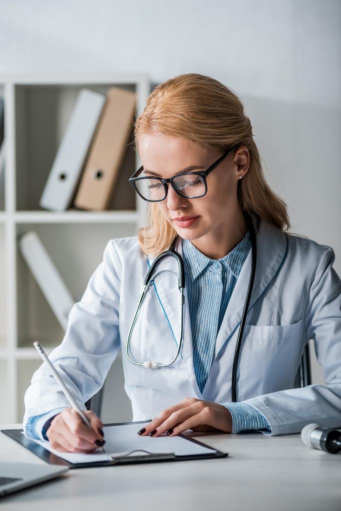 médico bonito em óculos escrevendo diagnóstico na clínica
  - Foto, Imagem