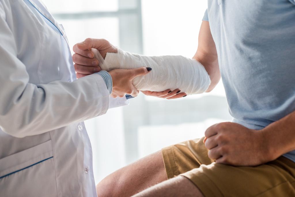 vista recortada del ortopedista tocando brazo herido del hombre
  - Foto, imagen