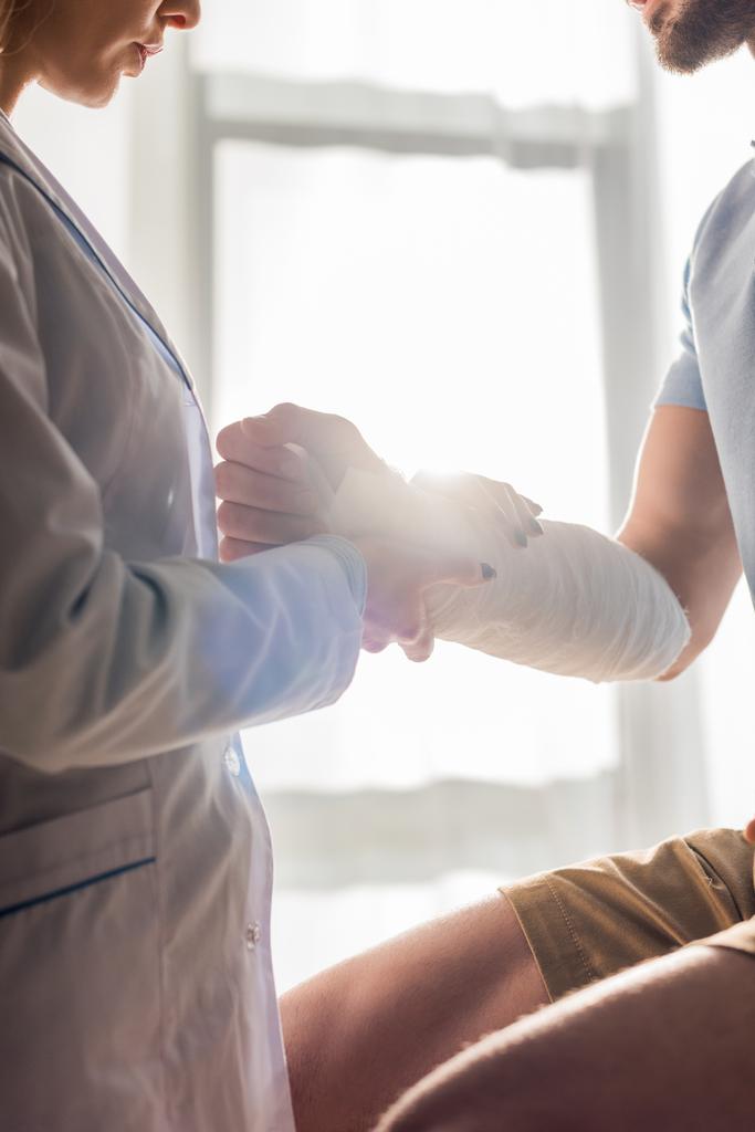 bijgesneden mening van orthopeed aanraken gewonde hand van de mens in kliniek  - Foto, afbeelding