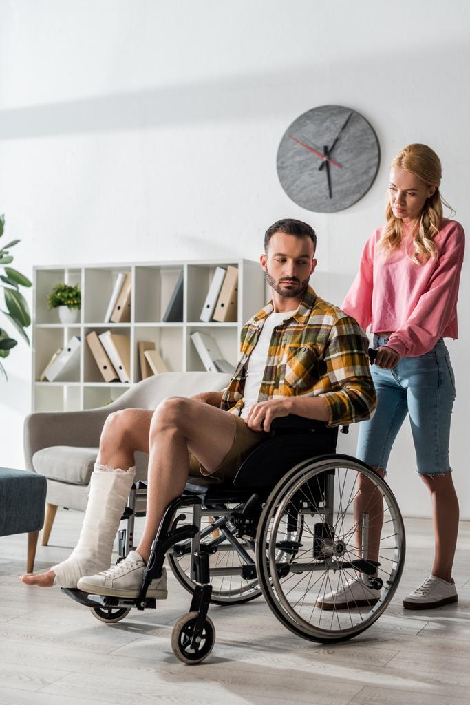 atrakcyjna kobieta stoi w pobliżu brodaty mężczyzna siedzi na wózku inwalidzkim  - Zdjęcie, obraz