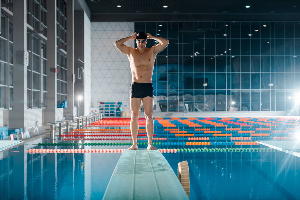 przystojny i muskularny pływak dotykający czepka przy basenie  - Zdjęcie, obraz