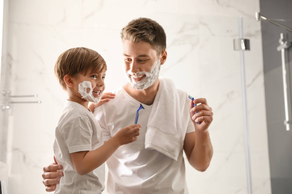 Papa en zoon met scheerschuim op hun gezicht hebben plezier in bad - Foto, afbeelding