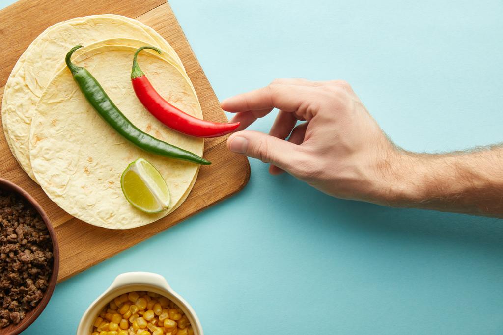 Top nézet-ból ember gazdaság chili paprika-val tortillák, darált hús és tortillák kék háttér - Fotó, kép