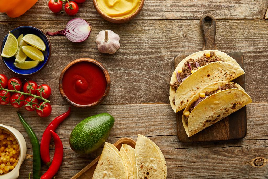 Top view of tacos on cutting board with fresh ingredients on wooden background - 写真・画像