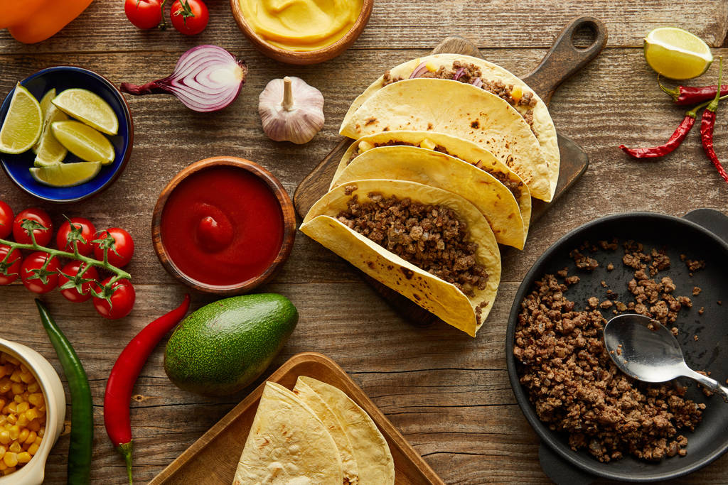 Top view of minced meat, tacos and raw ingredients on wooden background - Photo, Image