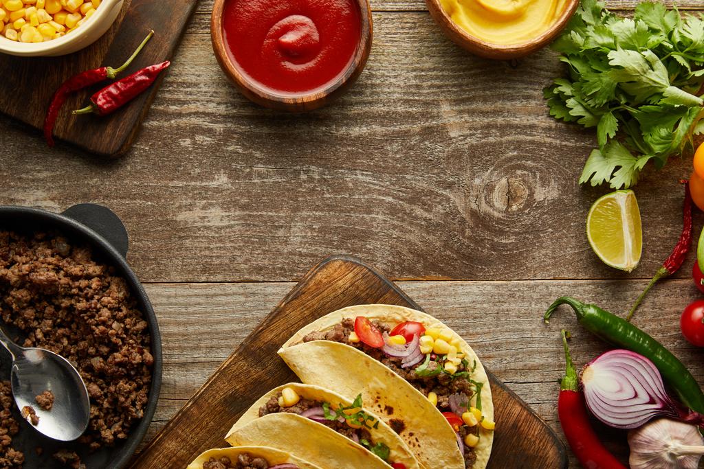 Top view of tasty tacos with minced meat and fresh ingredients on wooden surface - 写真・画像