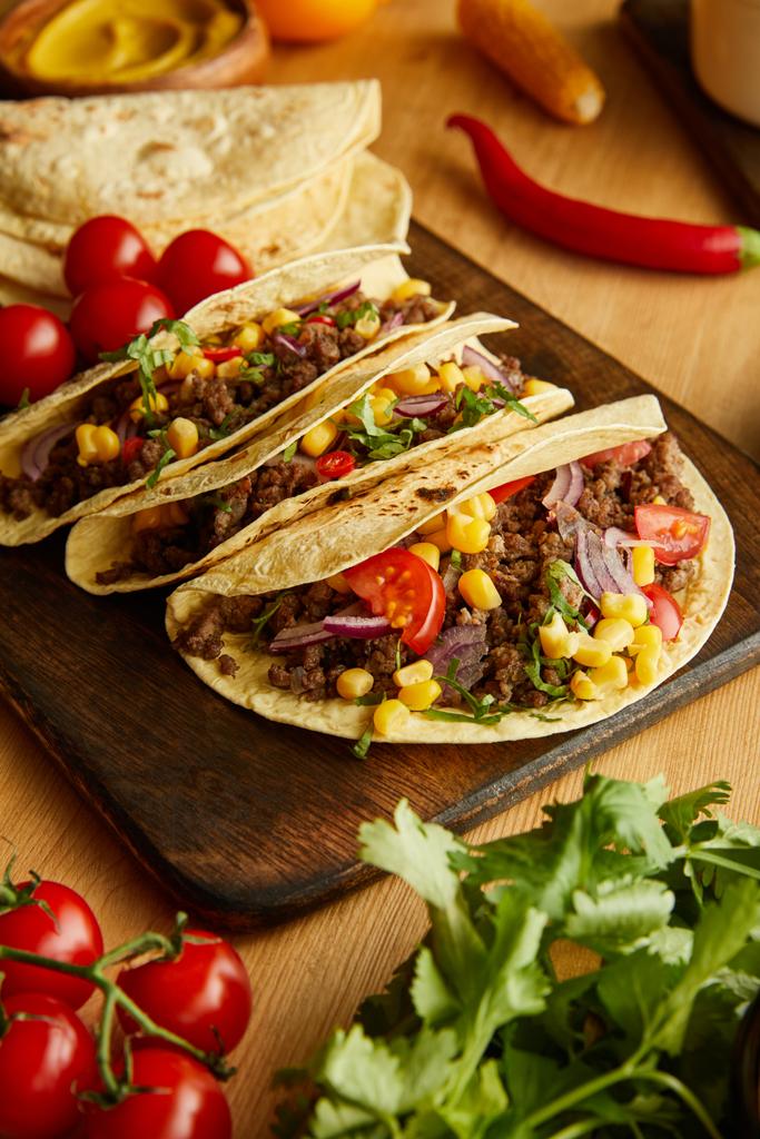 Delicious tacos with ripe vegetables and greenery on wooden table - Photo, Image