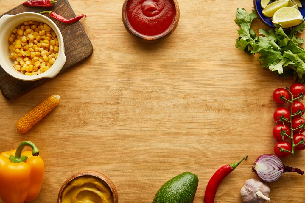 Vista superior de verduras orgánicas con ketchup y mostaza en cuencos sobre superficie de madera
 - Foto, Imagen